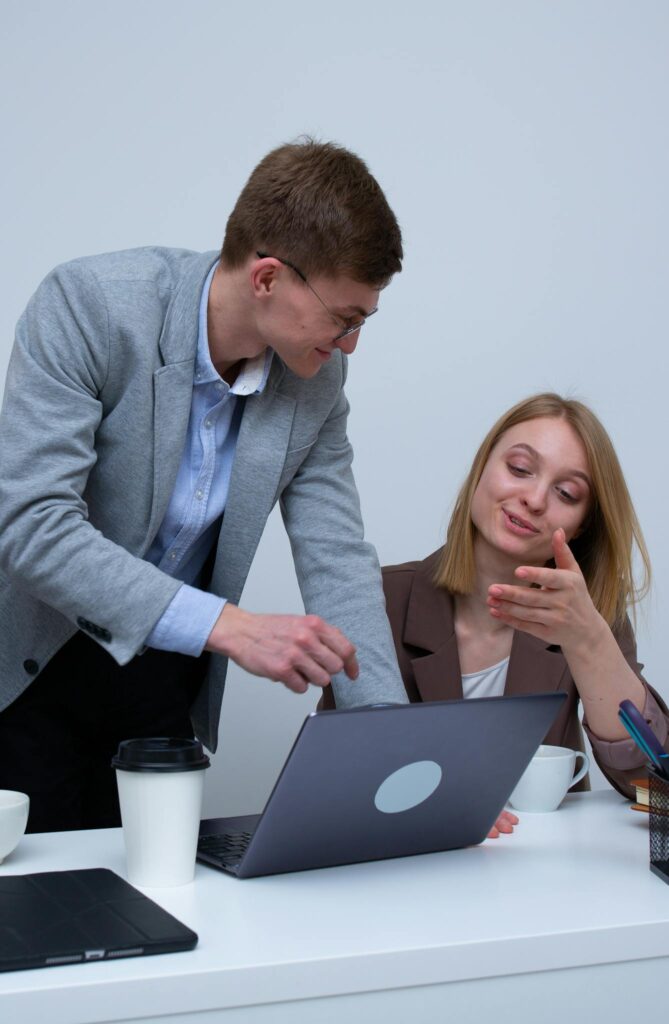 Two colleagues collaborating over laptops in a modern office setting.